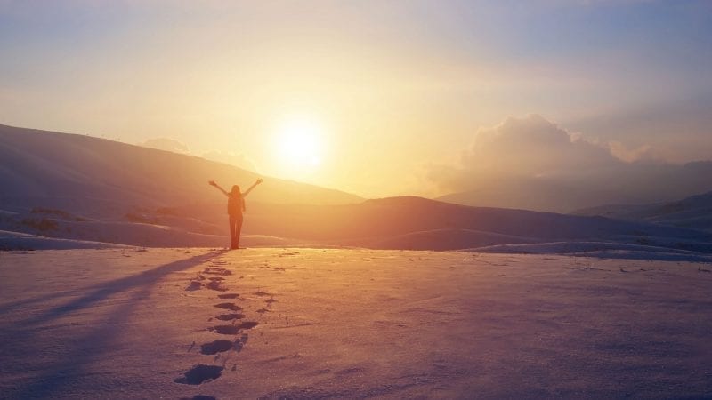 Eine Frau in bergiger Schneelandschaft schaut in die Sonne